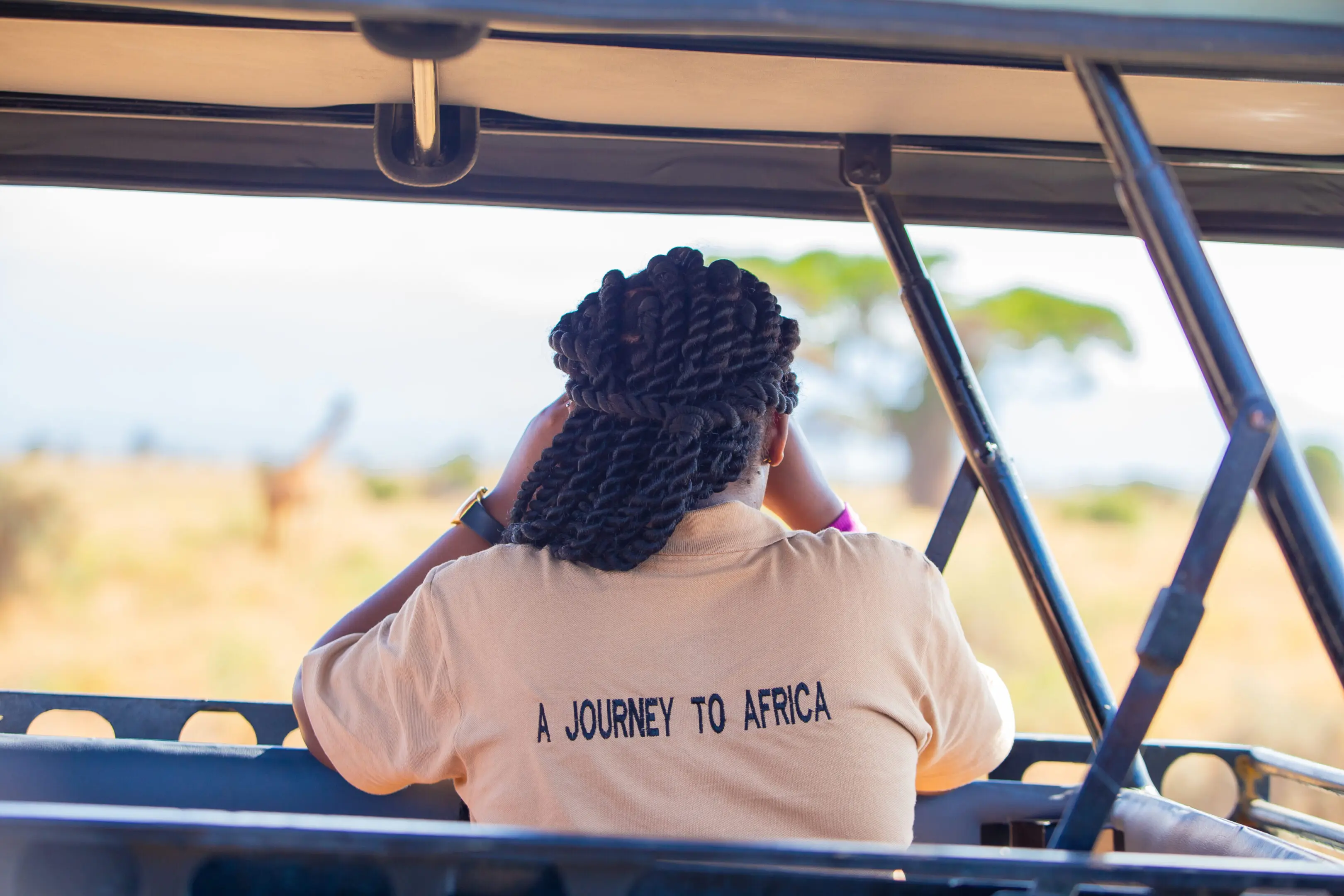 Person wearing a shirt that says 'A JOURNEY TO AFRICA' sitting in a vehicle.