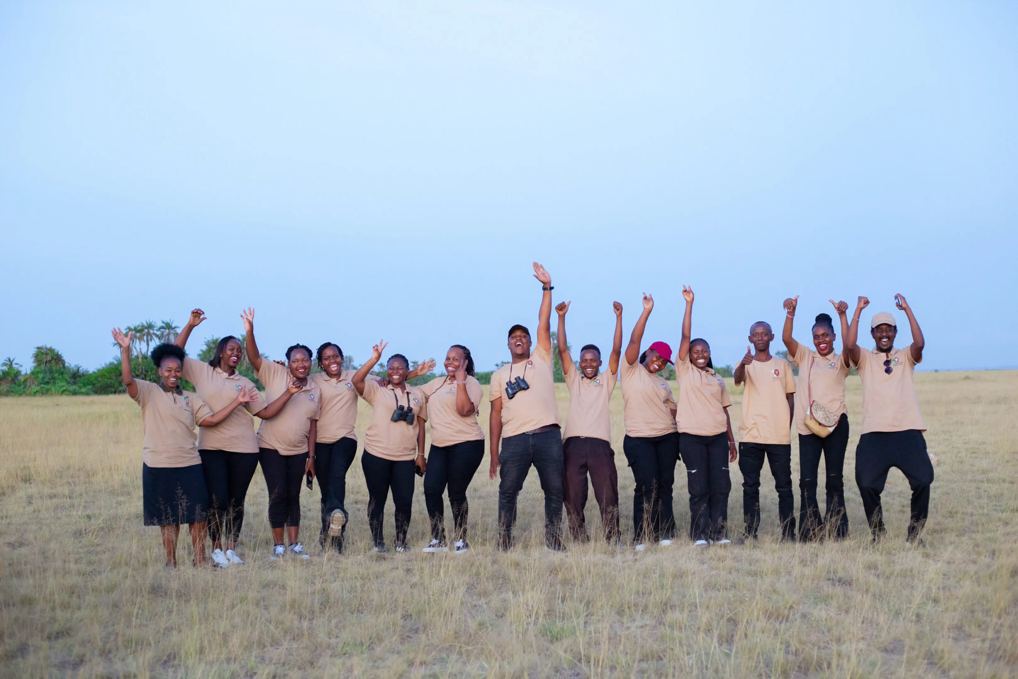 Group of people standing on a field with hands raised joyfully.
