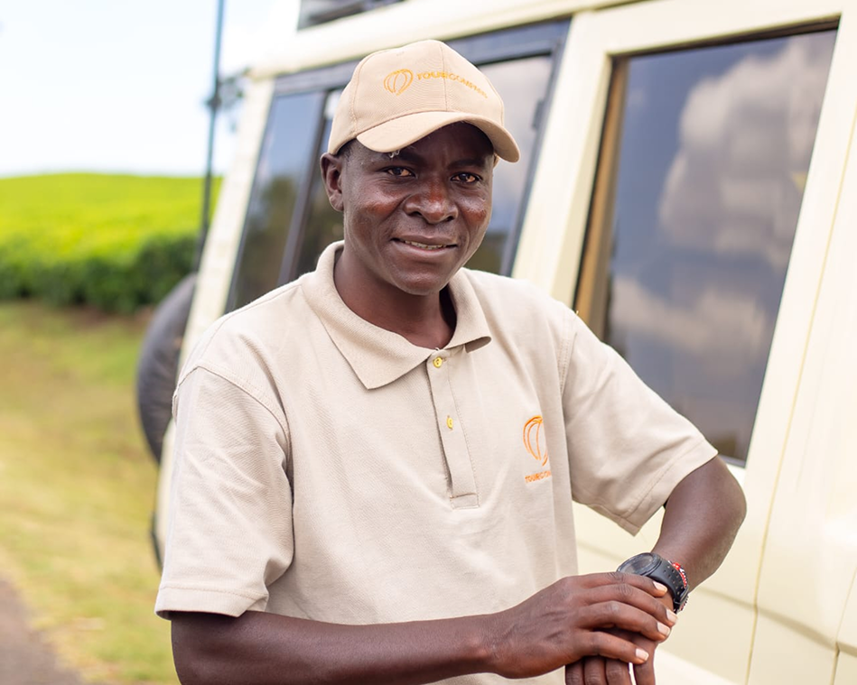 Man in a beige polo and cap smiles outdoors near a vehicle.