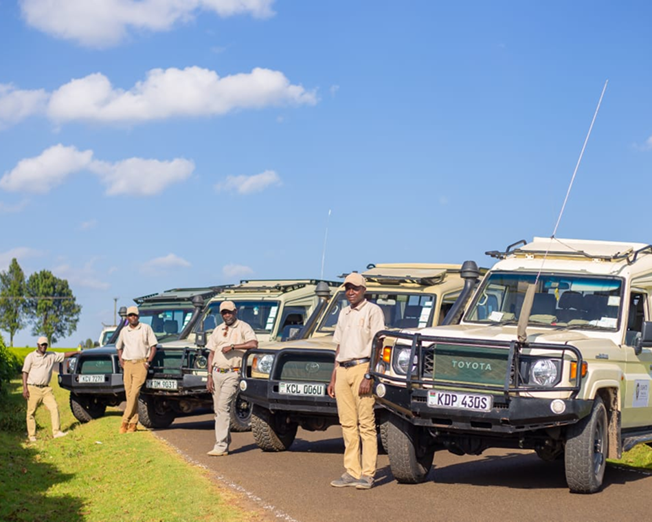 Uniformed officers standing beside a lineup of safari vehicles under a blue sky.